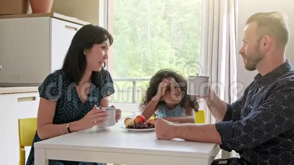 美丽的家庭和孩子坐在桌子旁在新家喝咖啡围着纸板箱视频的预览图