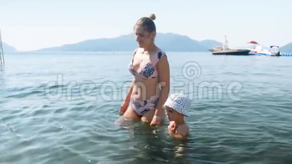 4k视频微笑的年轻母亲和小男孩在阳光明媚的日子在海上行走视频的预览图