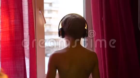 年轻人站在窗边跳舞用耳机听音乐他喜欢听音乐视频的预览图