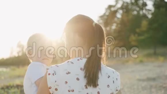 一位年轻的母亲抱着一个小儿子在日落女孩和小儿子身边散步视频的预览图