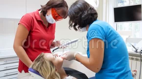 牙科医生在病人牙齿上涂上光聚合物后护士拿着紫外线灯4k镜头视频的预览图