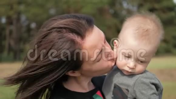 幸福的家庭在大自然户外母亲亲吻小男孩在绿色的草地上视频的预览图