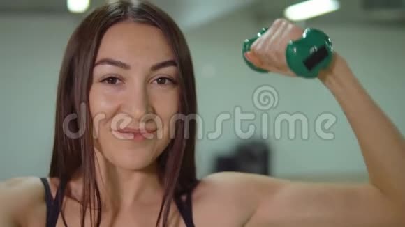 一位年轻的美女在健身房锻炼时用哑铃做特写视频的预览图
