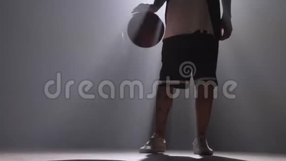 一名篮球运动员带着泛光灯在昏暗的房间里运球视频的预览图