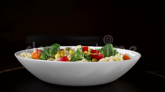 盘上有蔬菜的螺旋面在黑色背景上旋转视频的预览图