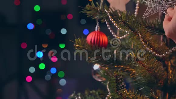 一位女士在圣诞树叶子上挂着圣诞装饰上面有闪闪发光的LED视频的预览图
