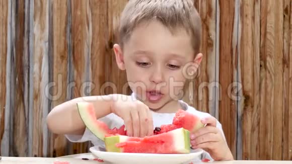 一个小男孩坐在桌子旁吃了一个多汁的红色西瓜视频的预览图