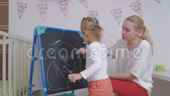 妈妈教小女孩用粉笔在黑板上画画视频的预览图