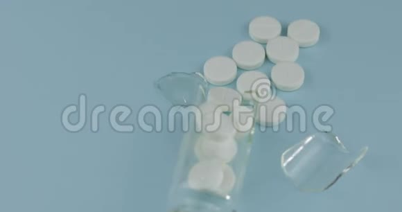 破碎的玻璃罐里面有许多药丸和药物在蓝色背景下旋转视频的预览图