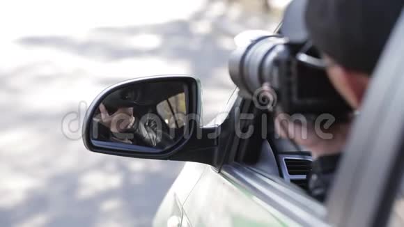 年轻的私家侦探坐在车里用数码相机拍摄侧镜的倒影视频的预览图