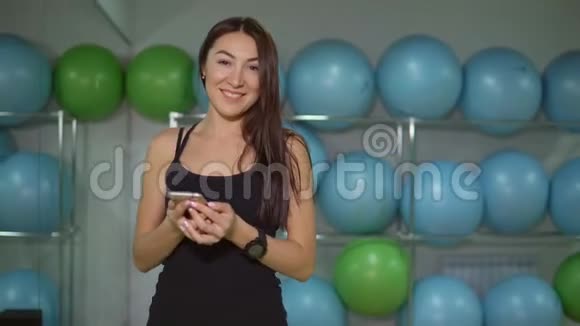 穿着运动服的年轻女子带着健身房体操球背景的电话视频的预览图