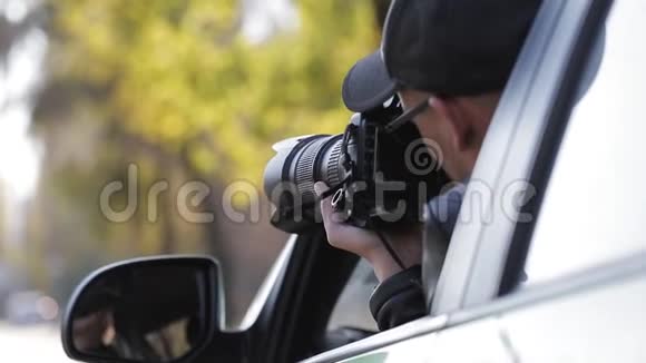 年轻的私家侦探坐在车里用数码相机拍摄侧镜的倒影视频的预览图