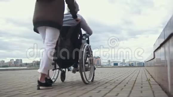 女人载着一个残疾人坐轮椅走在街上视频的预览图