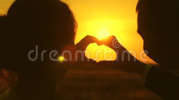 恋爱中的情侣用手展示心形符号新郎新娘在美丽的夕阳下用手做一颗心视频的预览图