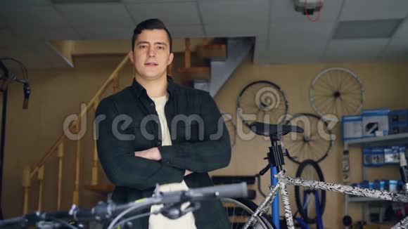 年轻英俊的职业机械师双手交叉站在自行车修理车间的画像视频的预览图