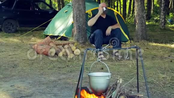 一个人坐在帐篷里喝茶看着一个保龄球挂在火上视频的预览图