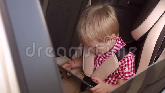 一个五岁的小男孩坐在汽车座椅上玩平板电脑视频的预览图