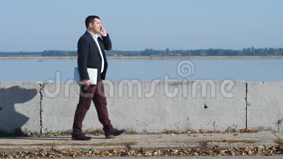 一个穿西装的男人在河边打电话视频的预览图