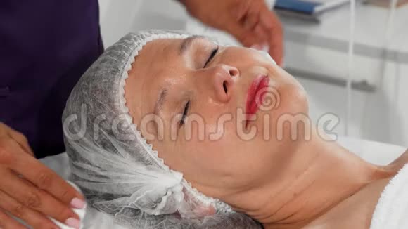 当美容师用棉垫清洁她的脸时老妇人微笑着视频的预览图