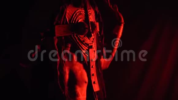 一个戴着木制面具的非洲男人和身上神秘的图案在红光中跳舞动作缓慢视频的预览图