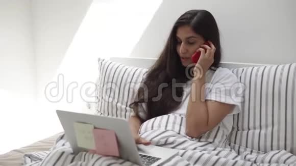 开朗的女人正在用笔记本和手机工作躺在床上视频的预览图