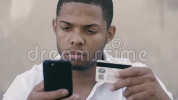年轻的非洲男人在线银行使用智能手机购物与信用卡视频的预览图