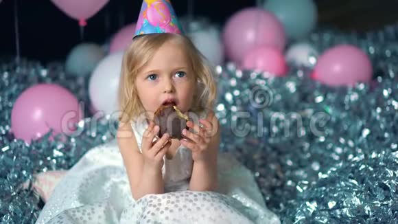 美丽快乐的小女孩咬生日蛋糕看着摄像机视频的预览图
