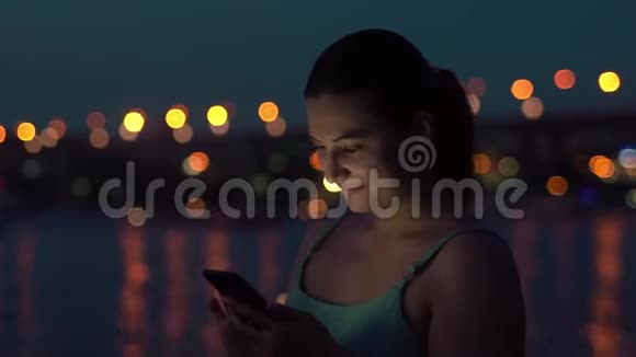一个女孩晚上在城市里散步时使用智能手机心情很好视频的预览图