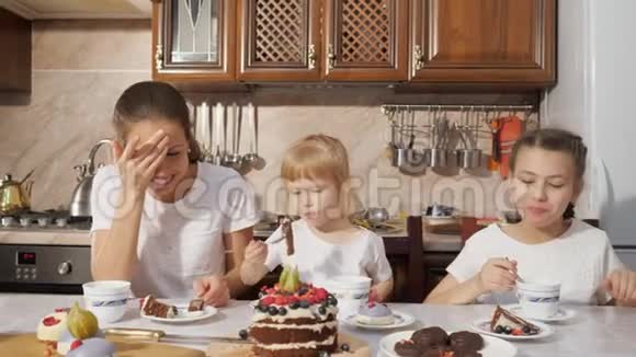 妈妈和两个女儿正在厨房里喝一杯带自制巧克力蛋糕的茶家里过生日视频的预览图