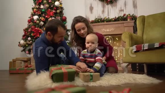 妈妈爸爸和小宝宝坐在房间的地板上一家人一起庆祝圣诞节视频的预览图