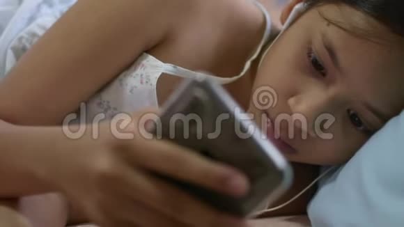 可爱的女孩从手机听音乐耳机躺在床上视频的预览图
