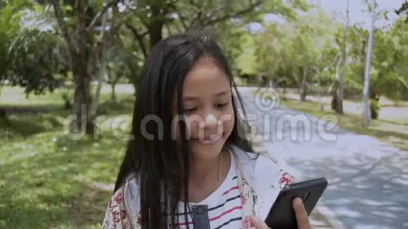 可爱的女孩用手机在公园里散步视频的预览图