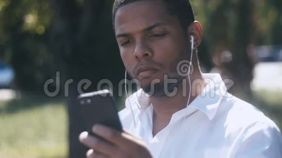 年轻商人的肖像使用智能手机在城市户外用耳机听音乐视频的预览图