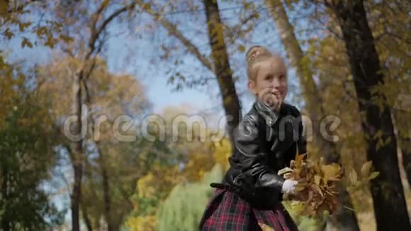 可爱的快乐学校女孩把落叶扔了起来在秋天的森林里玩美丽的女孩在玩视频的预览图