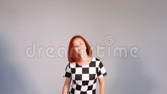 漂亮快乐的红头发女孩穿着花纹连衣裙在演播室里跳舞和跳跃视频的预览图