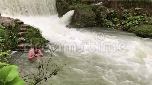 一个成年人在瀑布脚下沐浴着清爽的水视频的预览图