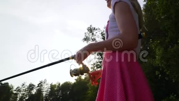 金发少女渔夫正在森林湖上钓鱼拿着鱼竿扭动着线圈妇女视频的预览图