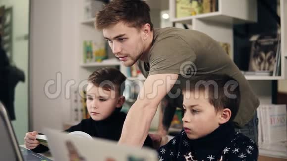 两个男孩和他们的年轻男性程序员老师在教室里学习如何使用笔记本电脑的录像替代办法视频的预览图