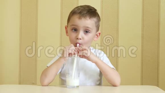 一个快乐的孩子通过吸管从杯子里喝牛奶表现出快乐和一只手的拇指视频的预览图