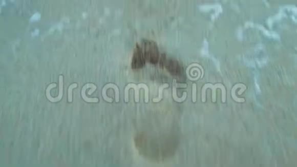 特写镜头穿着橙色衣服的光脚女人在潮湿的沙滩上留下的脚印视频的预览图