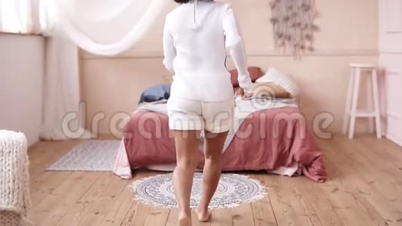 一段美丽的年轻女子穿着时髦的白色服装在床上翻筋斗视频的预览图