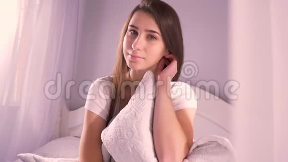 在室内卧室里轻轻抱着枕头的年轻白种人女性的特写肖像视频的预览图