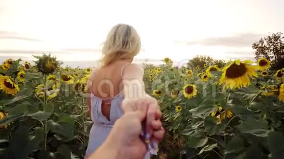 年轻的金发女郎穿着一件轻便的衣服穿过向日葵的田野走向地平线黄色花瓣的美丽花朵视频的预览图