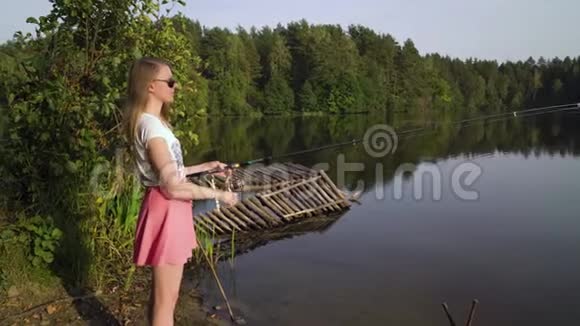 金发少女渔夫正在森林湖上钓鱼拿着鱼竿扭动着线圈妇女视频的预览图