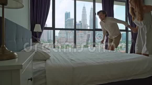 一对年轻夫妇在蜜月旅行中跳上床的慢镜头床垫和枕头概念视频的预览图