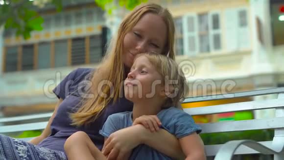 马来西亚槟城乔治城的一个老地方年轻女子和儿子坐在广场的长凳上视频的预览图