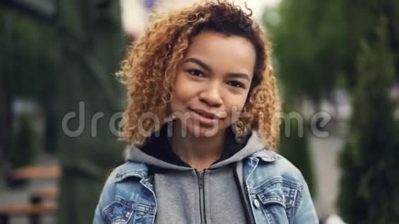幸福的非裔美国女人笑着看着镜头抚摸着站在公园里的头发视频的预览图