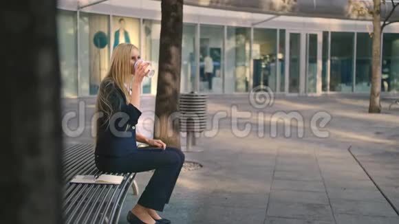 有咖啡和平板电脑的女人从侧面看正式的妇女坐在长凳上喝着咖啡视频的预览图