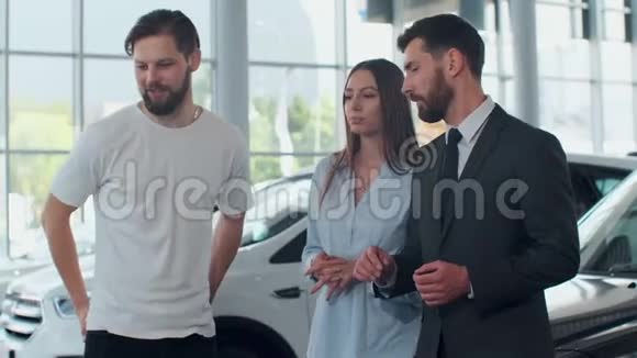 专业的汽车销售人员告诉有兴趣的买家美丽的一对夫妇在车展上豪华的汽车而男人和人视频的预览图
