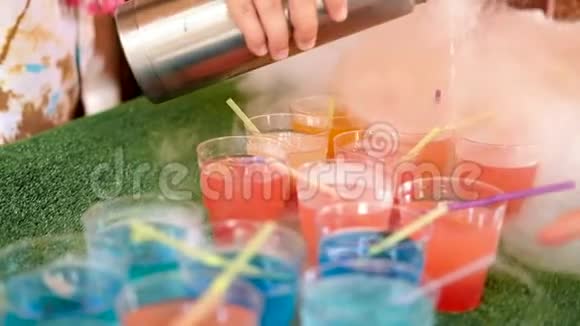 女酒保用手从热水瓶里倒出可吸烟的鸡尾酒多种颜色的带有管子的杯子站在绿色的背景上视频的预览图